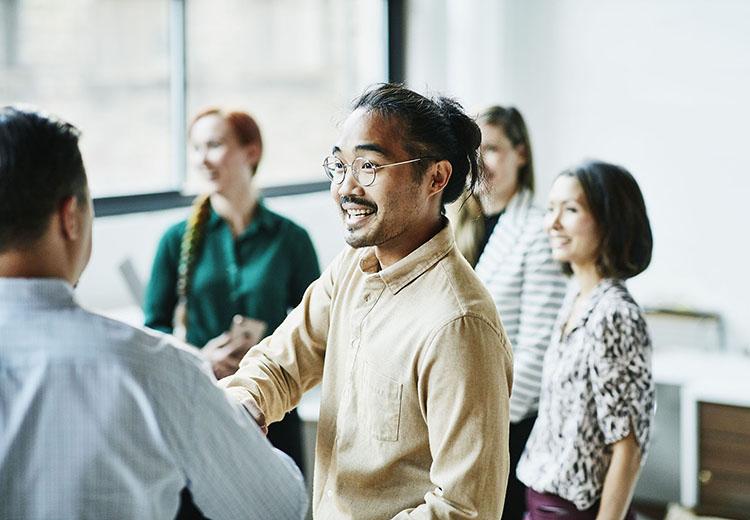 An Asian man smiling in a group of people indoors and shaking hands