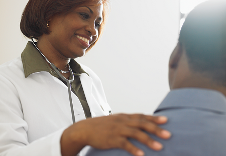 A smiling doctor with a stethoscope draped around her neck has hand on patient's shoulder