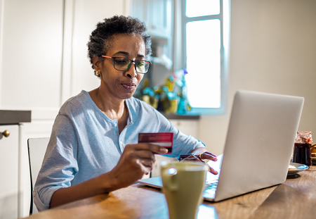 Older woman holding her credit card as she looks at her laptop, indicating she is purchasing something