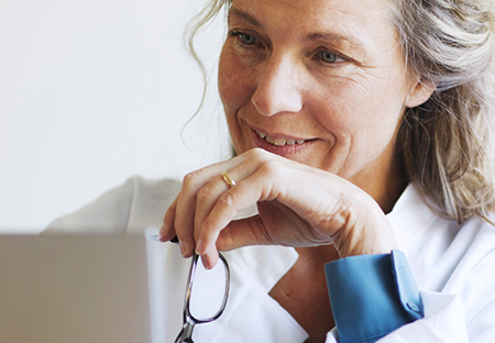 A woman smiling in front of a computer holding her glasses