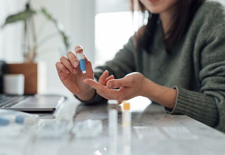 A closeup of a woman administering medicine to herself, about to prick her own finger