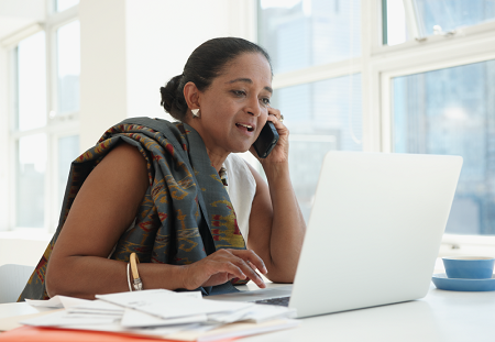 An elderly woman browses her laptop as she converses on the phone