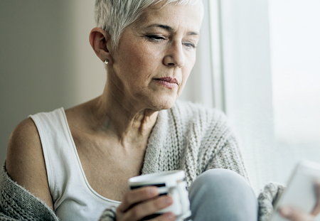woman holding pill bottle and looking at phone