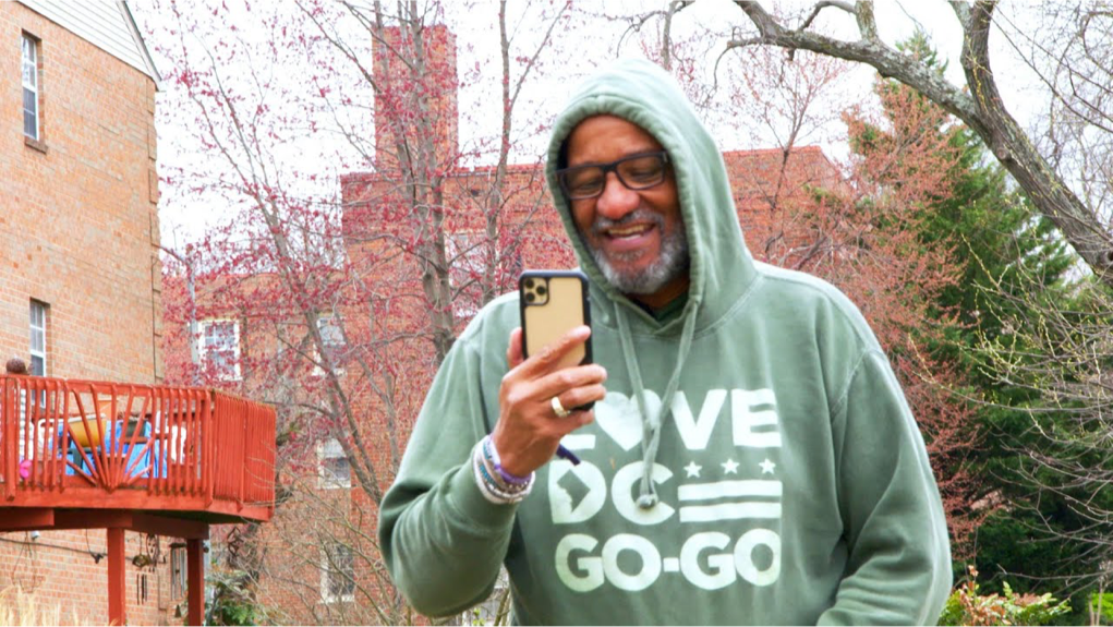 Watch on YouTube: Image of Lamont Mitchell walking outside, smiling and look at cell phone