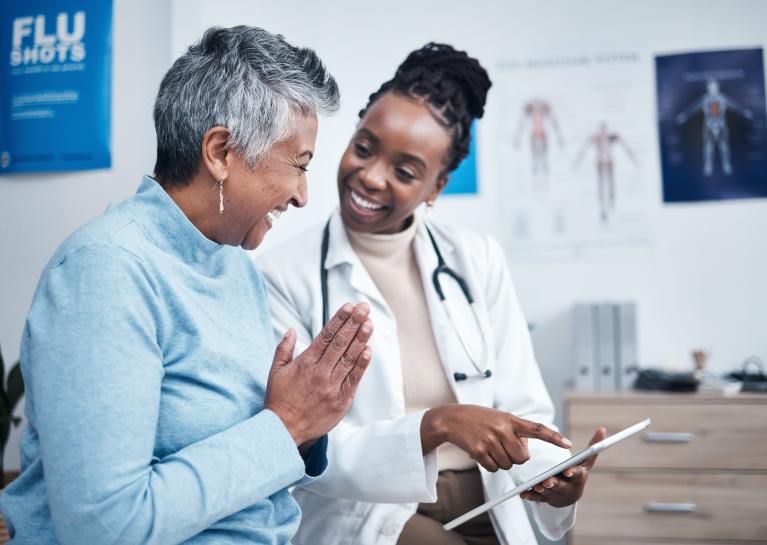 Image of a woman in a blue sweater smiling while speaking with a female healthcare provider in a white lab coat with a stethoscope